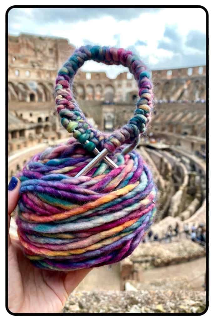 Colorful yarn with circular knitting needles sticking out of it photographed at the Colosseum in Rome, Italy.